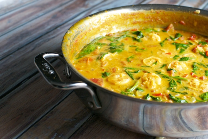 Rich shrimp and vegetable curry in a black skillet with vibrant colors, fresh herbs, and a flavorful, creamy sauce, served on a rustic wooden table.