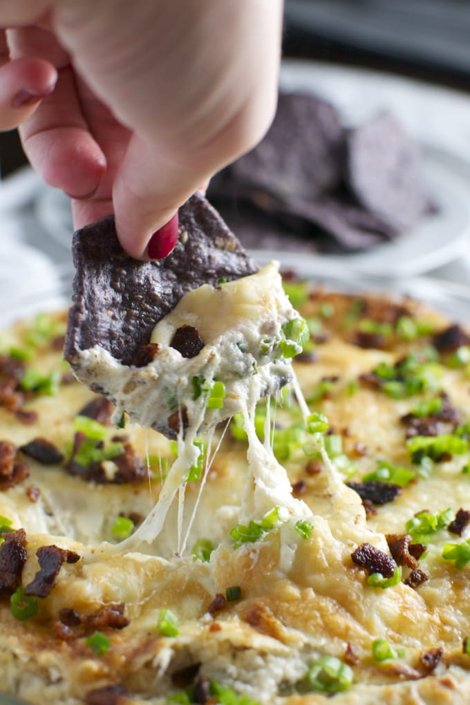 Golden, melted cheese pizza topped with crispy bacon and chopped green onions, served on a plate with a hand pulling a cheesy slice, showcasing gooey cheese and crispy toppings.