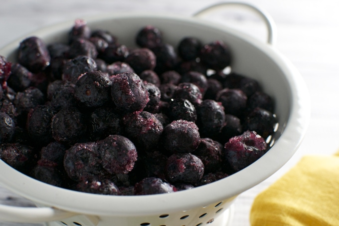 Fresh frozen blueberries in a white ceramic colander, perfect for healthy snacks and dessert ingredients.