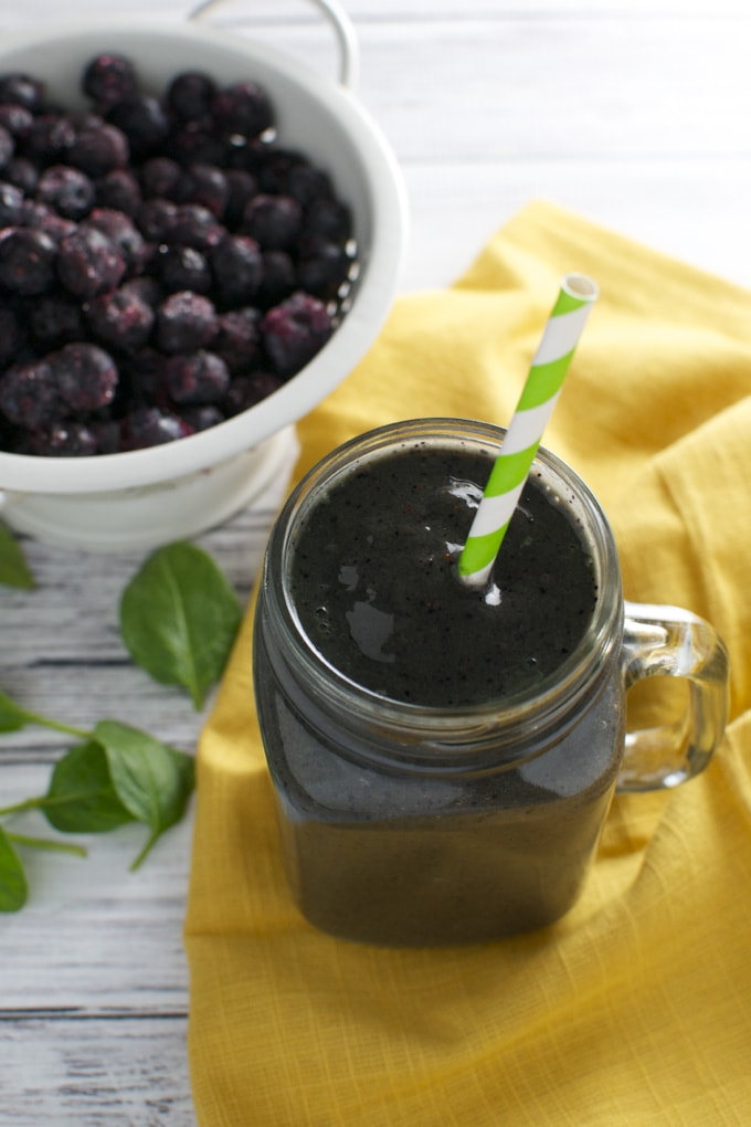 Fresh blackberry smoothie in a mason jar with a green-striped straw, served on a yellow cloth with a bowl of frozen blackberries, perfect for healthy desserts and berry lovers.