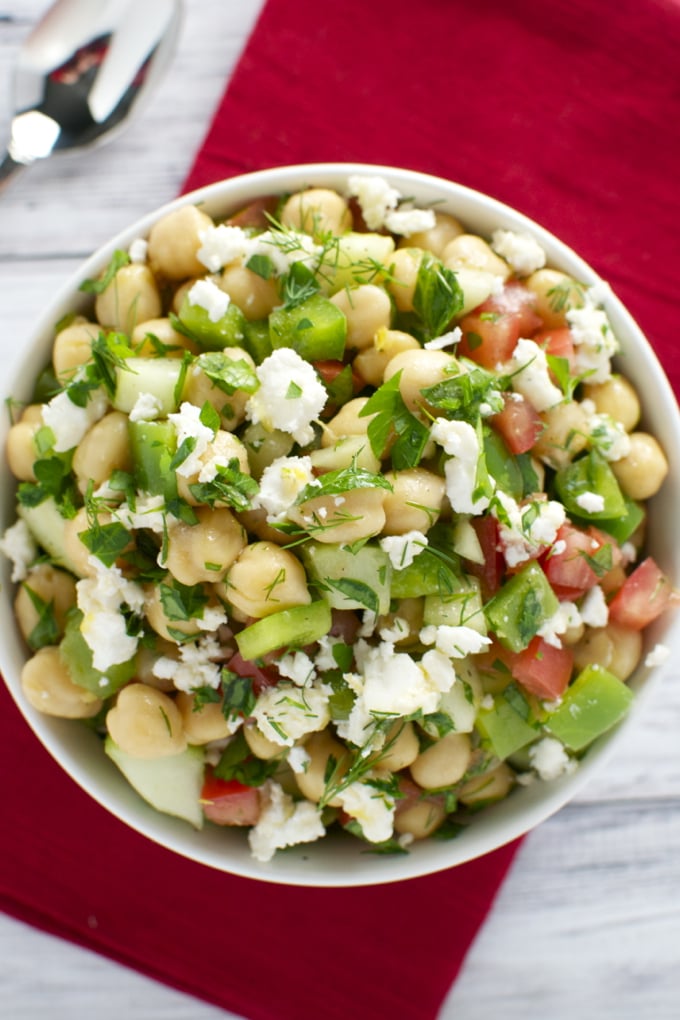 Fresh chickpea salad with diced cucumbers, tomatoes, feta cheese, and herbs in a white bowl.