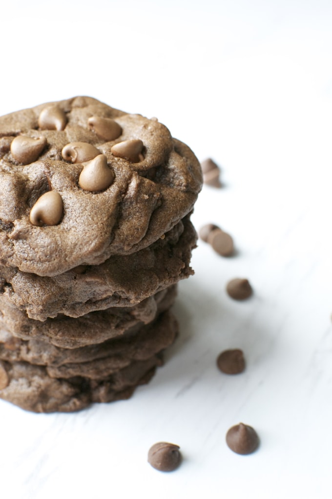 Chocolate chip cookies stacked with scattered chocolate chips on a white surface, appealing homemade treat from Stuck On Sweet. Perfect for dessert lovers and cookie enthusiasts.