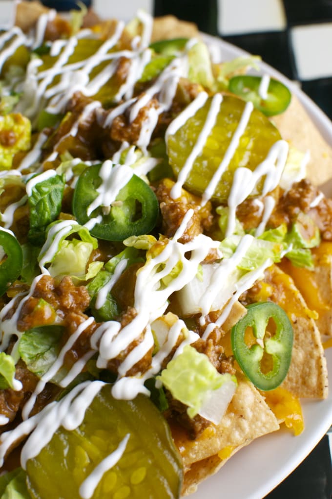 Crunchy taco salad with seasoned ground beef, fresh lettuce, sliced jalapeños, pickles, shredded cheese, drizzled with sour cream, served on a white plate.