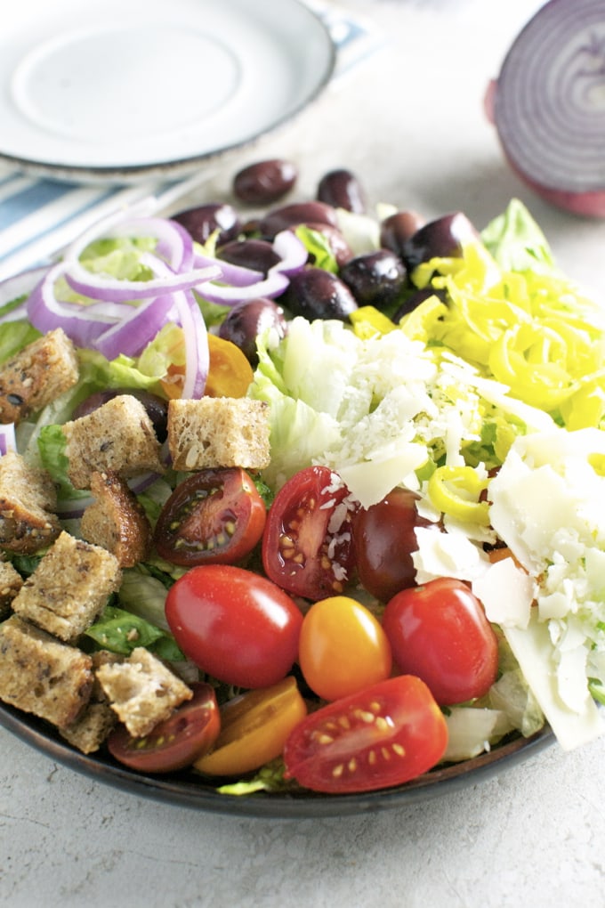 Fresh vegetable salad with cherry tomatoes, red onions, cucumbers, croutons, and shredded cheese on a dark plate, perfect for healthy eating and side dishes.