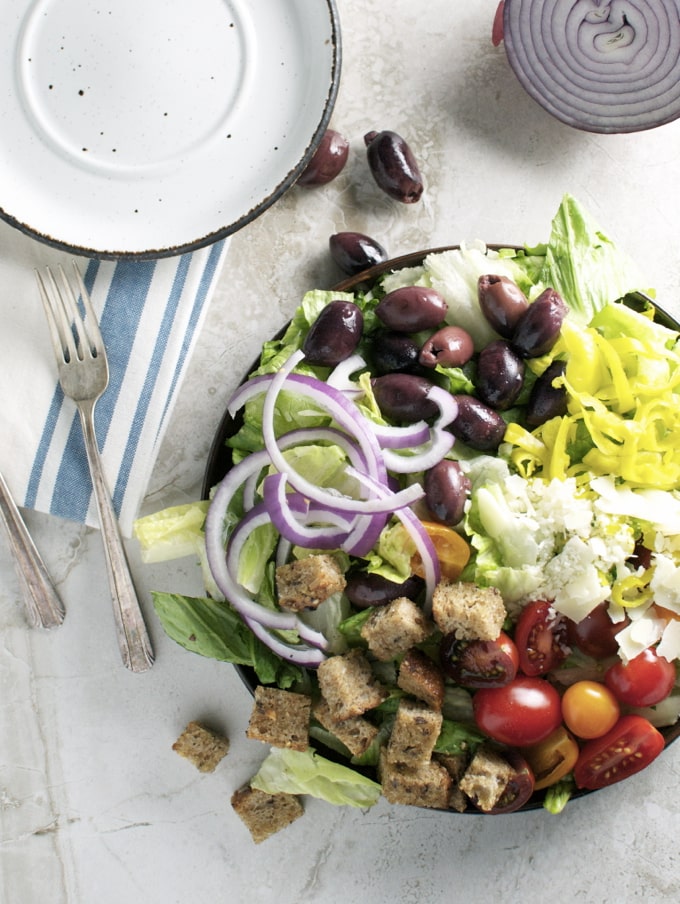 Fresh Greek salad with black olives, cherry tomatoes, red onions, cucumbers, lettuce, croutons, and feta cheese served on a white plate. Perfect for healthy eating and Mediterranean cuisine.