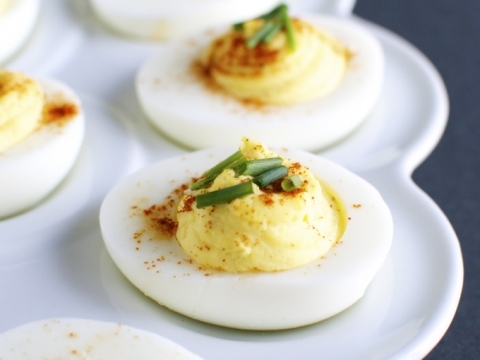 Creamy deviled eggs garnished with chives on a white platter, perfect for appetizers or party snacks. Elegant party appetizer, healthy snack, and holiday food presentation.