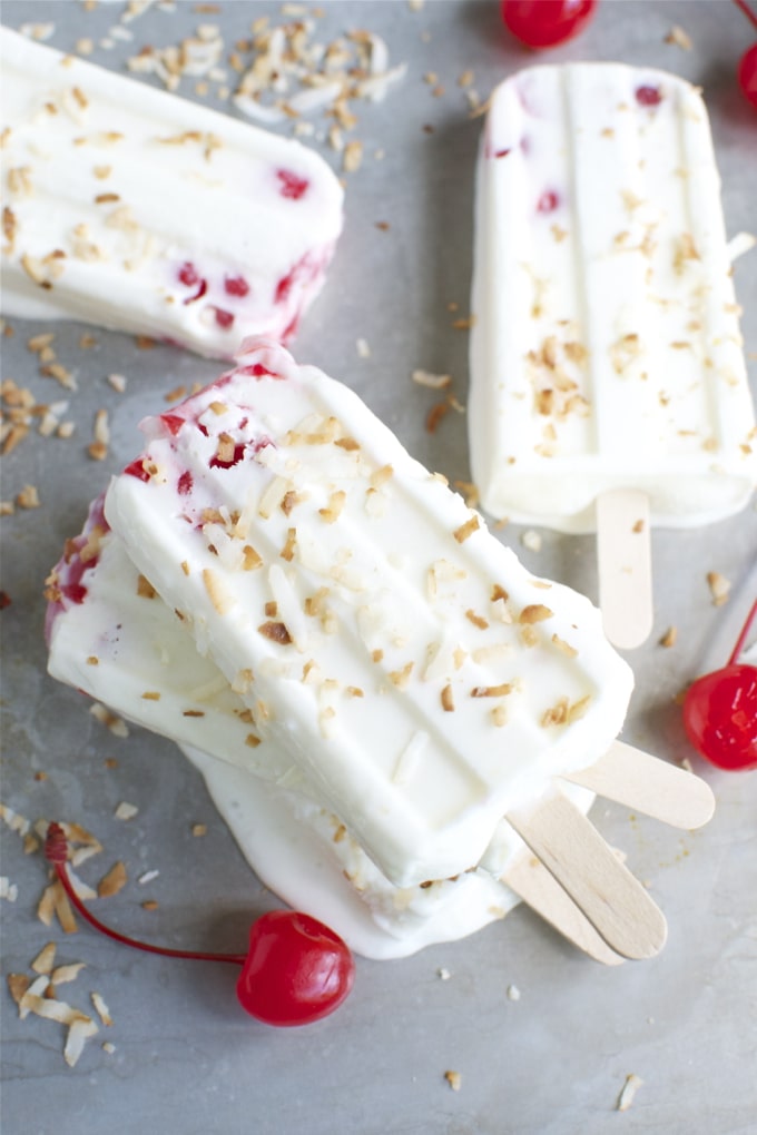 Creamy cherry ice cream bars with chopped nuts and fresh cherries on a chilled surface, perfect for summer treats. Delicious frozen desserts from Stuck On Sweet.