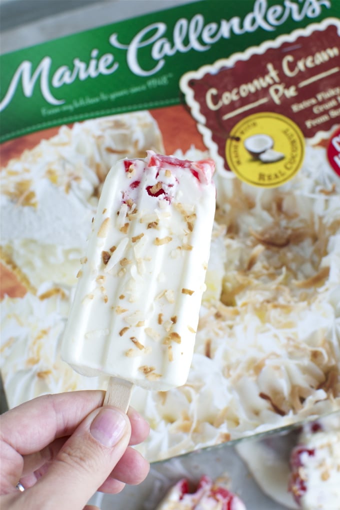 Creamy coconut ice cream bar sprinkled with toasted coconut flakes on a wooden stick.