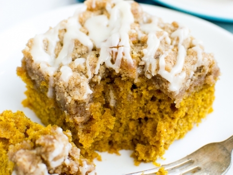 Moist pumpkin streusel coffee cake topped with cream cheese glaze on a white plate with a fork.