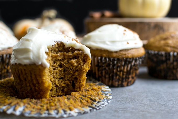 Moist pumpkin spice cupcake with cream cheese frosting on a rustic surface.