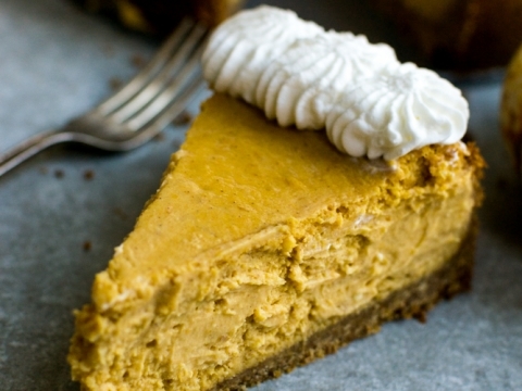 Creamy pumpkin cheesecake with a graham cracker crust topped with whipped cream, perfect for fall desserts. Available at Stuck On Sweet bakery, known for delicious baked goods.