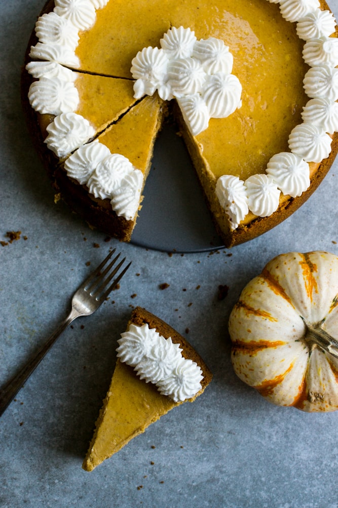 Rich pumpkin pie with whipped cream topping, served on rustic gray background for fall desserts and holiday treats.