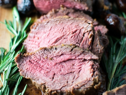 Juicy prime rib roast sliced on a wooden cutting board with fresh rosemary, seasoned to perfection, ideal for special occasions and family dinners.