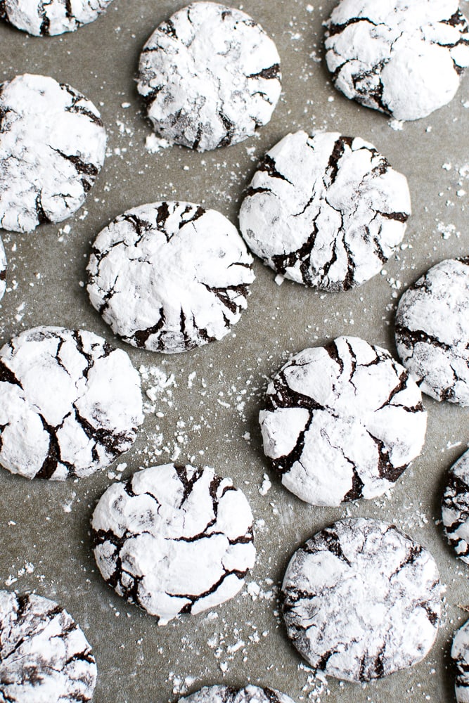 Crinkle cookies with powdered sugar and chocolate cracks on parchment paper.