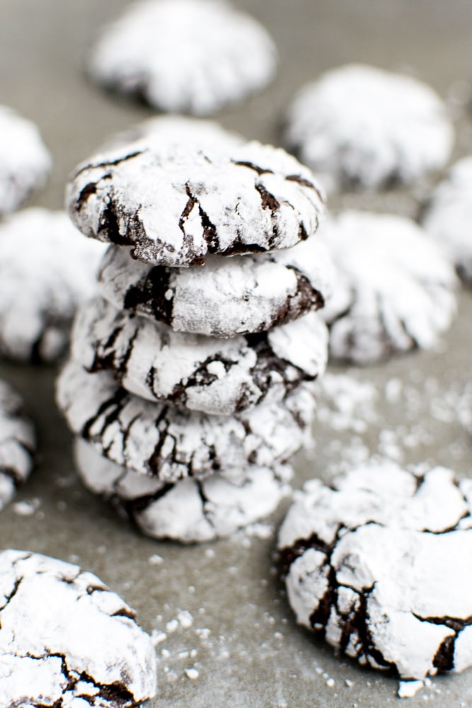 Crinkle cookies dusted with powdered sugar stacked on a gray surface with more cookies in the background.
