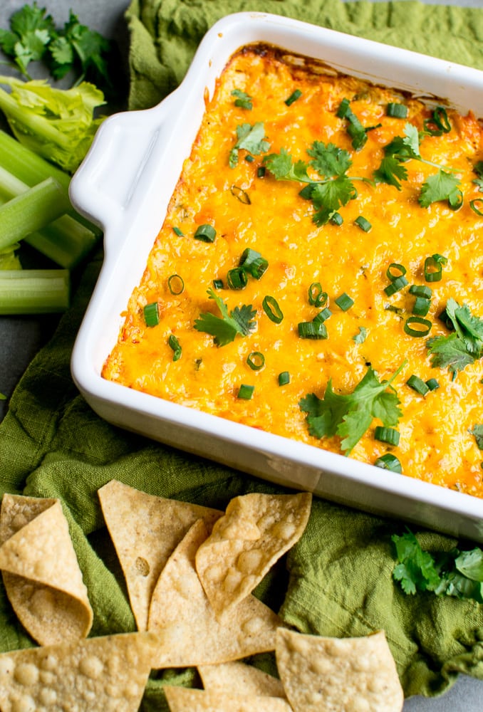 Cheesy buffalo chicken dip garnished with fresh herbs served with tortilla chips on a green cloth, perfect for dipping or a comforting side dish.