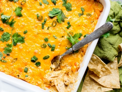Creamy buffalo chicken dip with melted cheddar, fresh cilantro, and green onions, served with crispy pita chips and celery sticks, perfect for family dinners or potlucks.
