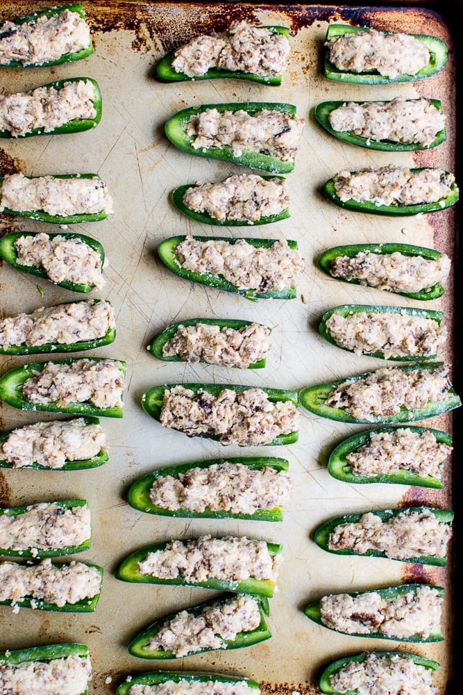 Green jalapeño peppers stuffed with creamy cheese filling, baked to perfection, on a baking sheet. Perfect appetizers for parties or snacking, combining spice and savory flavors.