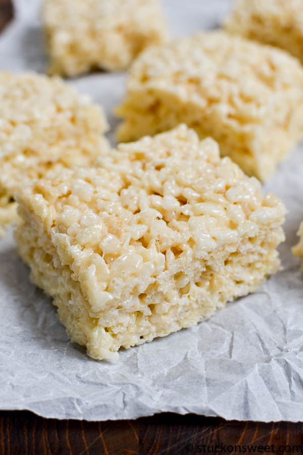 Chewy rice krispie treat square with marshmallow and butter, close-up on parchment paper background, homemade sweet snack.