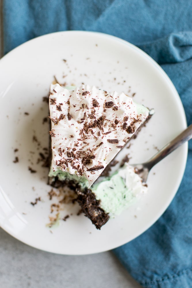 Creamy chocolate mint ice cream slice topped with whipped cream and chocolate shavings on a white plate, served with a spoon, perfect for dessert lovers.
