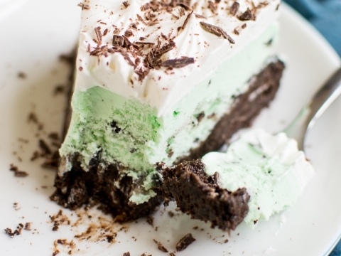 Creamy mint chocolate chip cheesecake with chocolate crust and whipped topping on a white plate. Perfect for dessert lovers and special occasions.