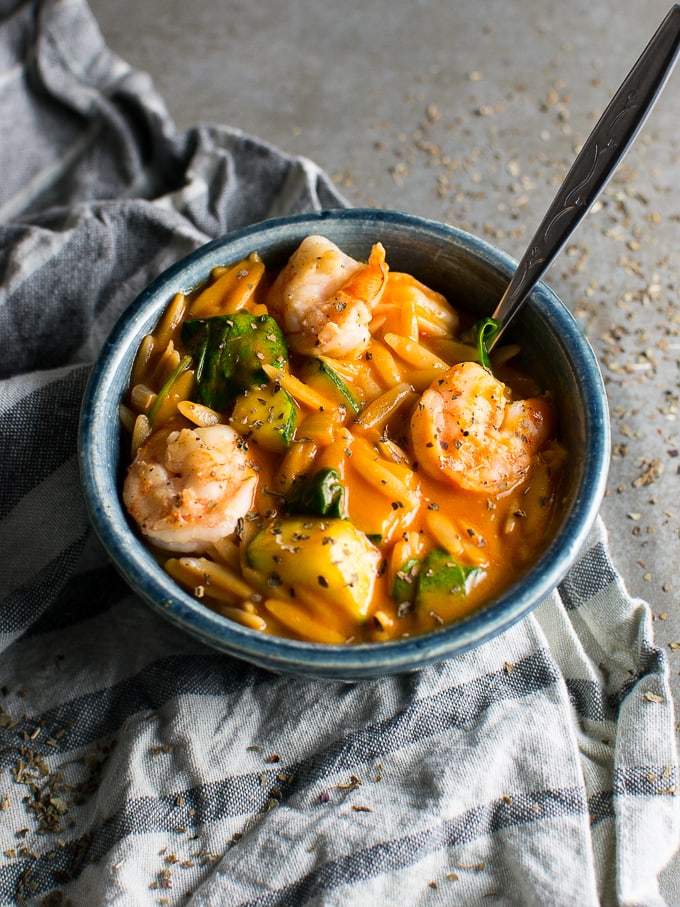 Savory shrimp and vegetable noodle soup in a blue bowl, served with a spoon on a rustic surface, featuring fresh ingredients and flavorful broth.