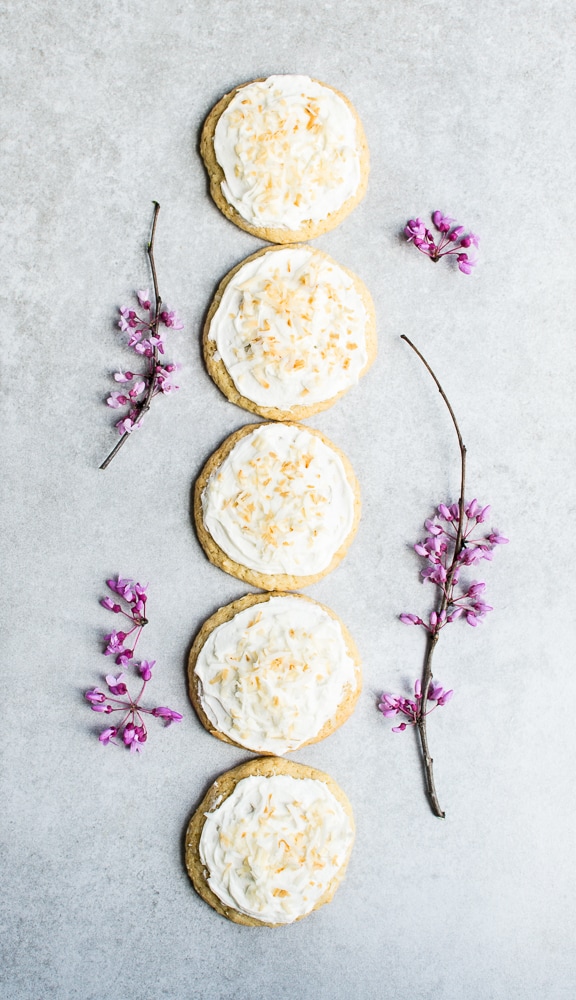 Cream cheese and shredded cheese-topped cookies arranged vertically with pink blossoms on a light gray surface.