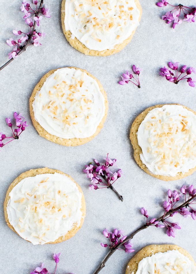 Delicious coconut cream frosted sugar cookies with shredded coconut topping on a light background with purple flowers.