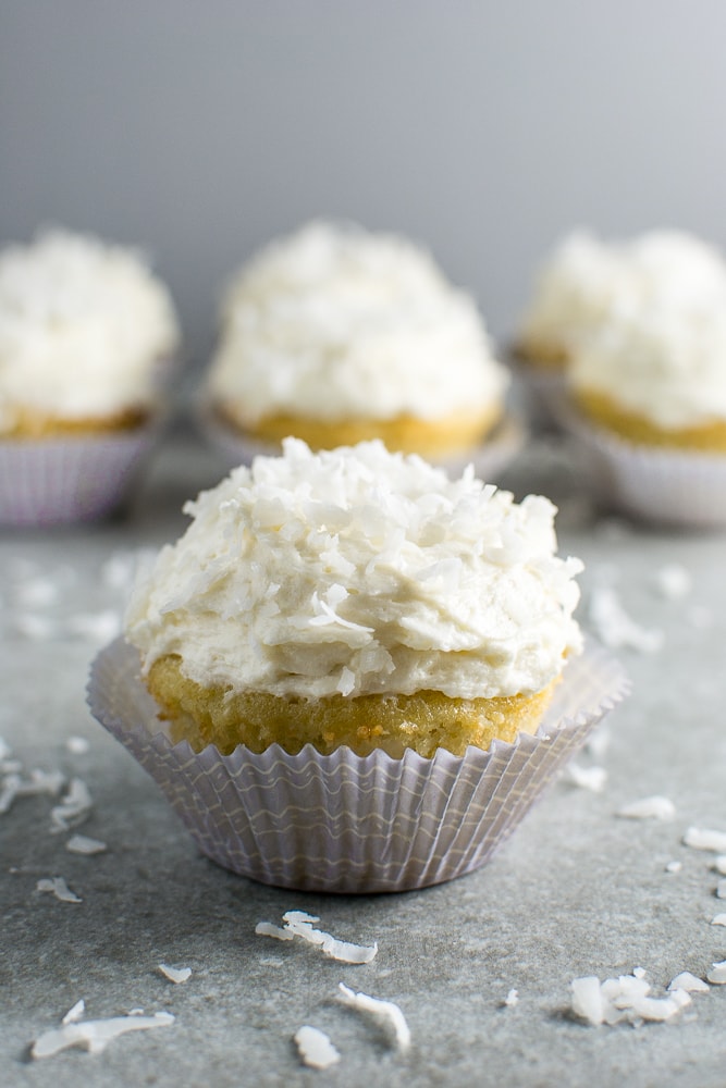 Cream cheese coconut cupcake with white frosting and shredded coconut, served in a paper cupcake liner. Perfect for dessert or special occasions.