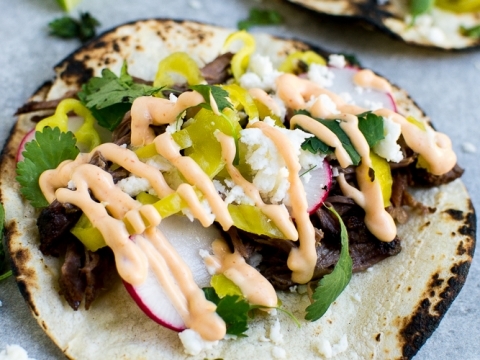Fresh grilled beef tacos with lettuce, radish, cilantro, and creamy spicy sauce on soft corn tortillas, served with lime wedges, perfect for Mexican cuisine lovers.