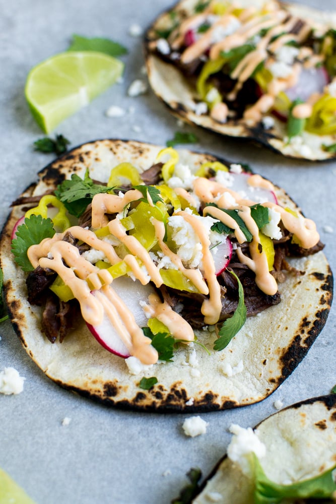 Fresh grilled beef tacos with lettuce, radish, cilantro, and creamy spicy sauce on soft corn tortillas, served with lime wedges, perfect for Mexican cuisine lovers.