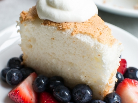 Creamy vanilla cheesecake slice topped with whipped cream, served with fresh strawberries and blueberries on a white plate. Perfect for dessert lovers and cheesecake enthusiasts.