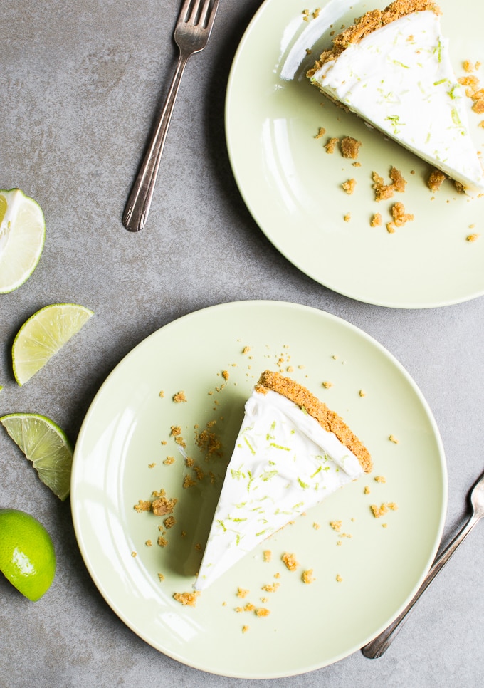 Lemon lime cheesecake slice with graham cracker crust on light green plates, fresh lime and lemon wedges, and silver forks, perfect for a citrus-inspired dessert.