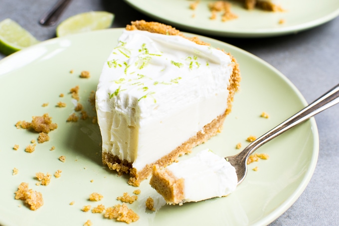Cream cheese lime pie on a green plate with lime wedges, topped with whipped cream, perfect for dessert lovers.