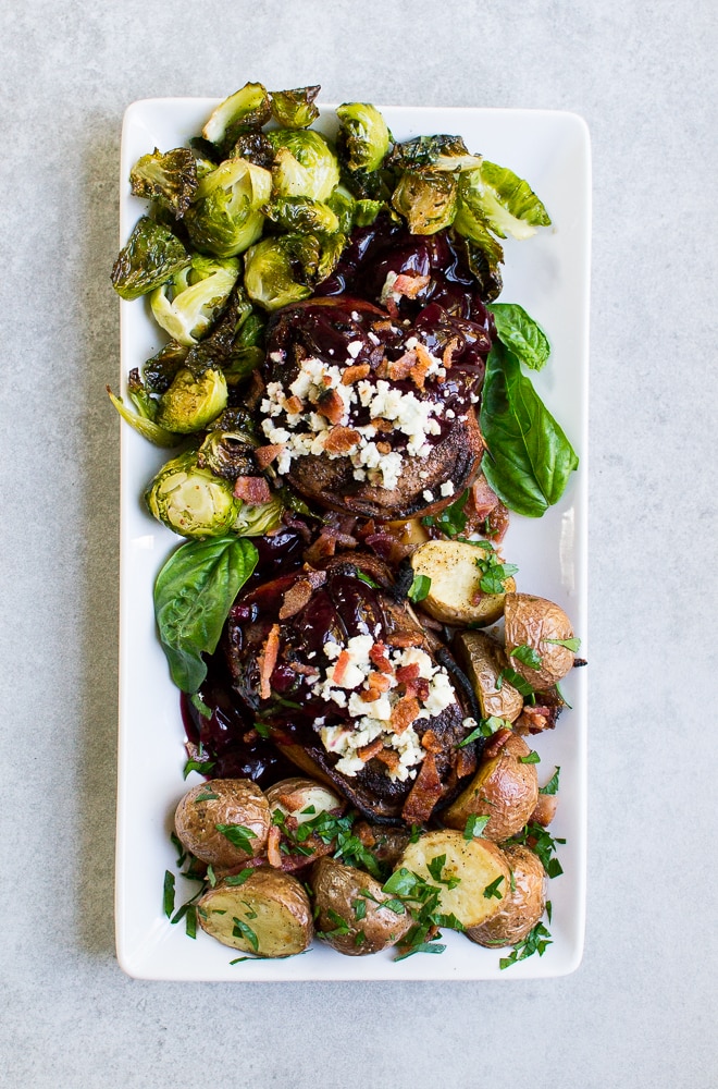 Roasted beef tenderloin with garlic roasted potatoes, Brussels sprouts, and fresh basil on a white rectangular plate.