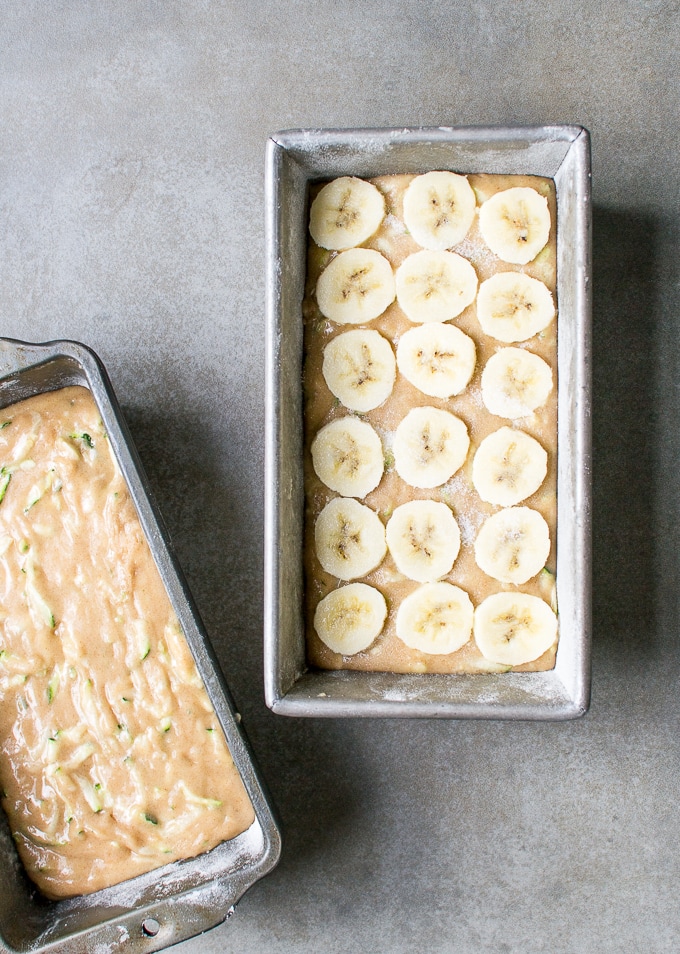 Sliced bananas on banana bread batter in a metal loaf pan, ready for baking.