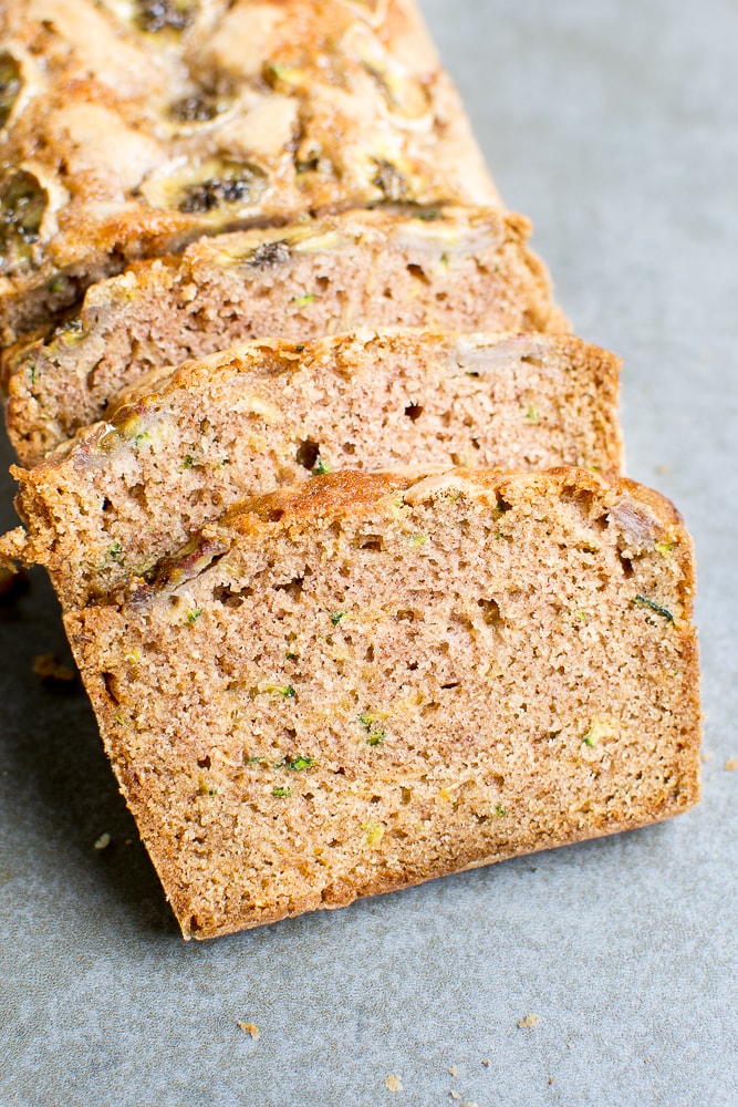 Rich banana bread with chocolate chips and chopped nuts, sliced and stacked on a gray surface, showcasing moist texture and delicious flavor.