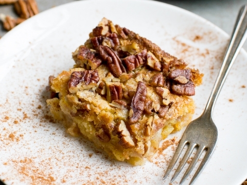 Apple Dump Cake on white plate with cinnamon spice, fork, and background of pecan nuts.