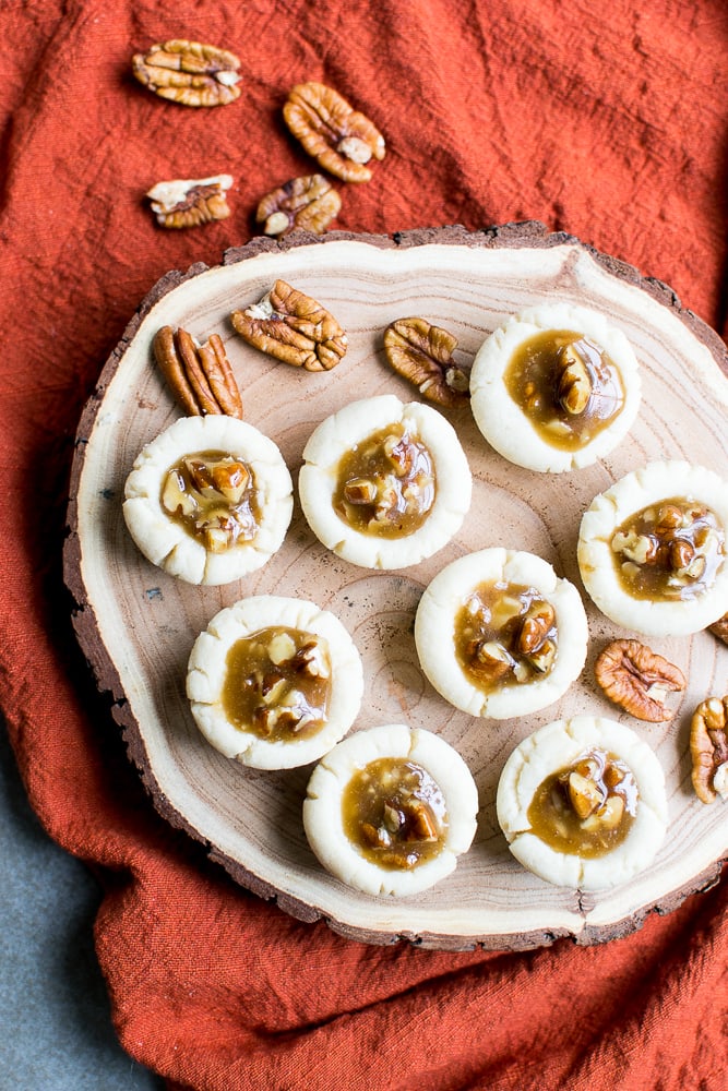 Creamy white chocolate pecan caramel cookies arranged on a rustic wooden platter with scattered pecans, perfect for sweet treat dessert or holiday snack.