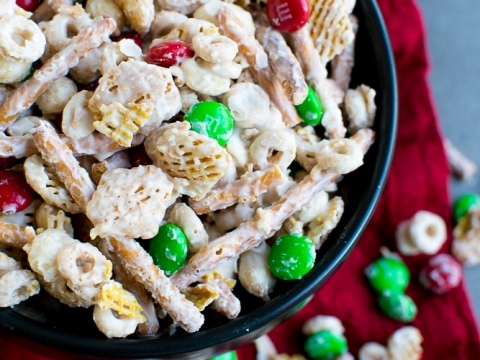 Colorful Christmas crack popcorn snack with M&M candies and caramel-coated popcorn in a black bowl on red cloth, festive holiday treat.
