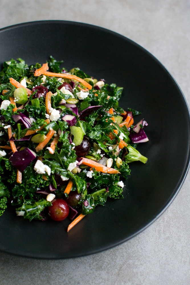 Fresh kale salad with grapes, carrots, cranberries, feta cheese, sunflower seeds, and a light vinaigrette, perfect for healthy meals and outdoor picnics.