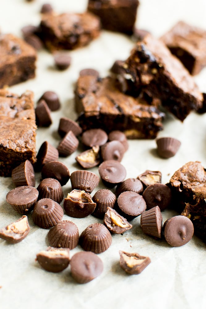 Rich chocolate brownie pieces with melted chocolate chips and chopped nuts, scattered with mini peanut butter cups, perfect for dessert or sweet snacking.
