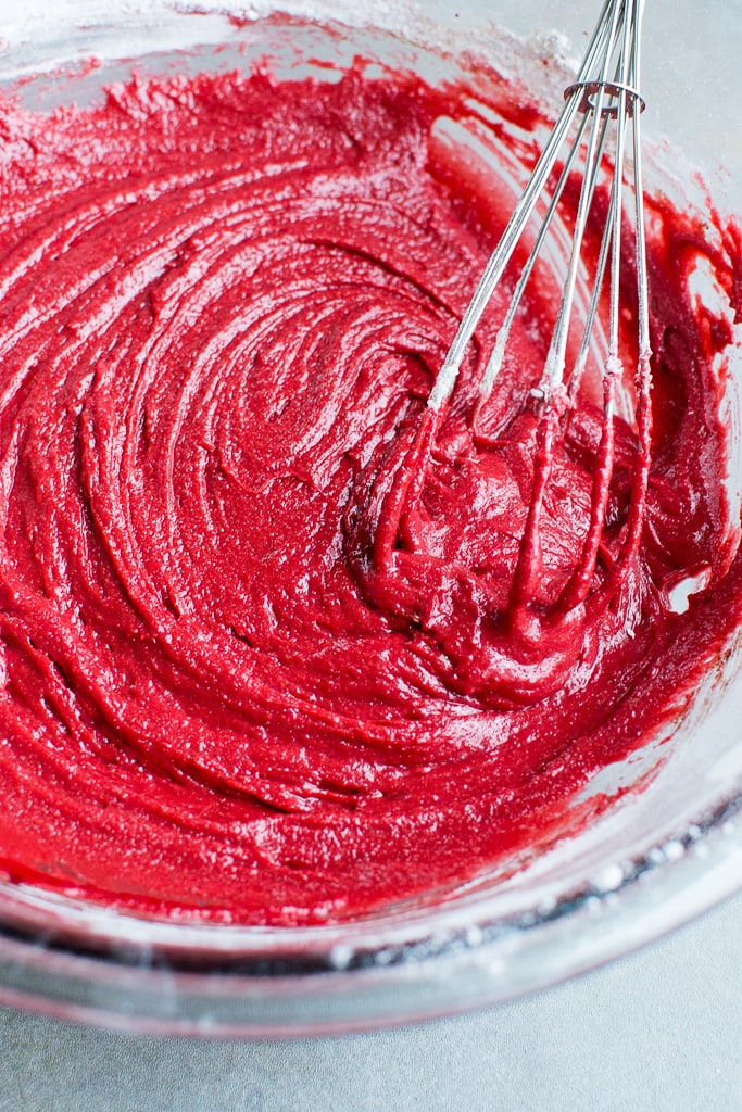 Sweet red cake batter mixture for baking, close-up of mixing in a metal whisk, perfect for cupcakes or cake recipes.