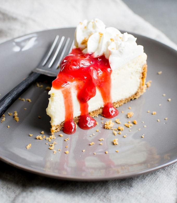Creamy cheeseburger cheesecake with cherry topping on a dark plate, topped with whipped cream, served with a fork. Perfect for dessert or special occasions.