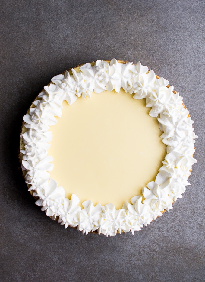 Creamy lemon cheesecake with decorative whipped cream border on a dark textured background.