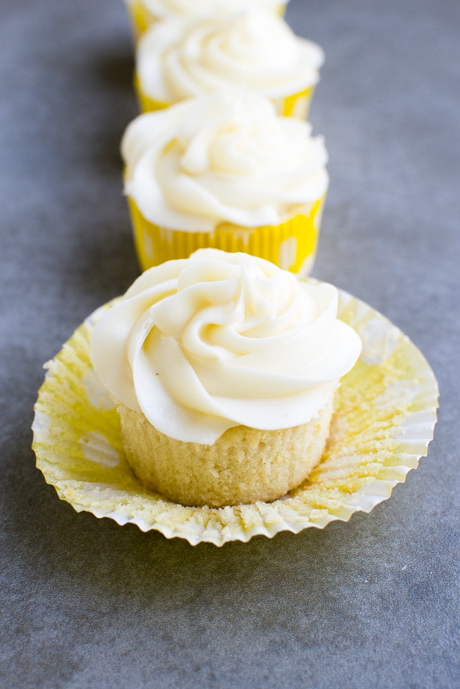 Rich vanilla cupcake with swirled creamy frosting and two lemon-flavored cupcakes in the background, perfect for dessert lovers.