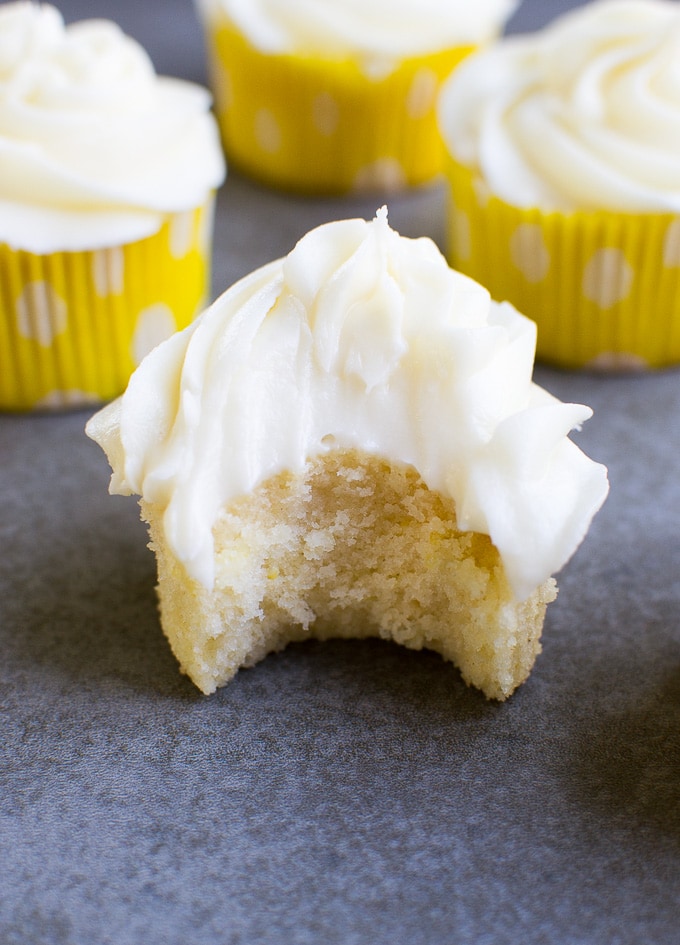 Bright yellow cupcake liners with white polka dots holding creamy vanilla cupcakes topped with swirls of vanilla frosting.