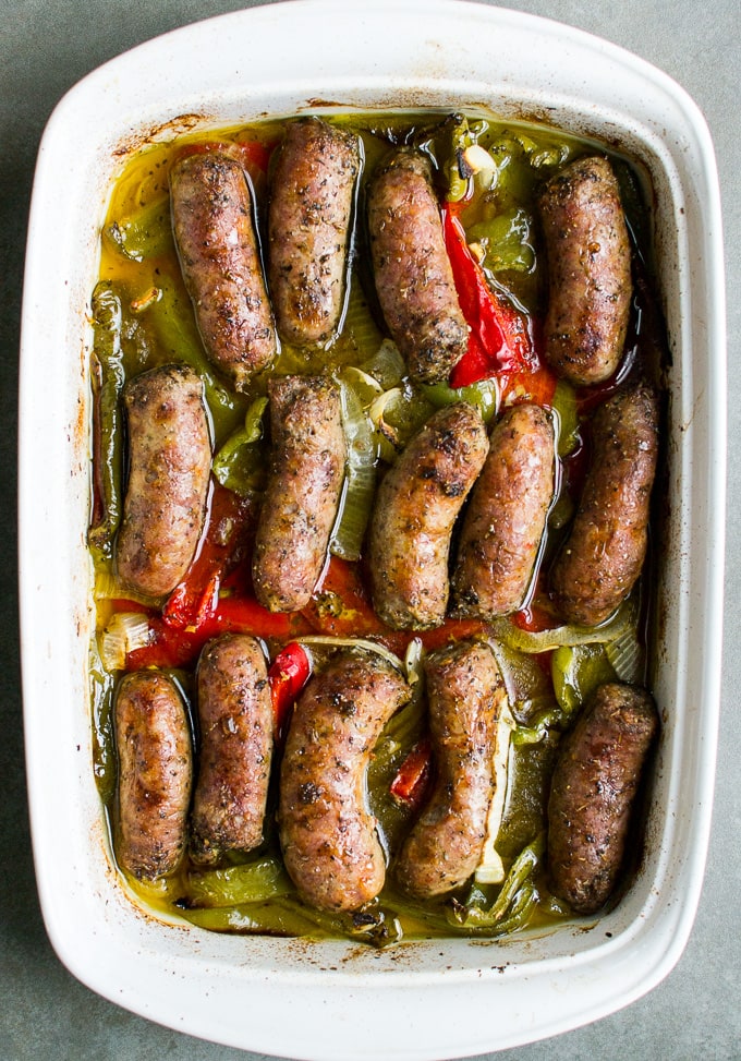 Juicy Italian sausage links baked with bell peppers and onions in a savory marinade, served in a white ceramic baking dish for a delicious, hearty meal.