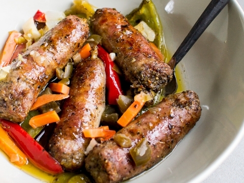 Savory Oven Baked Italian Sausage and Peppers with colorful chopped vegetables and herbs in a white bowl, served with a black fork, ideal for comforting home-cooked meals.