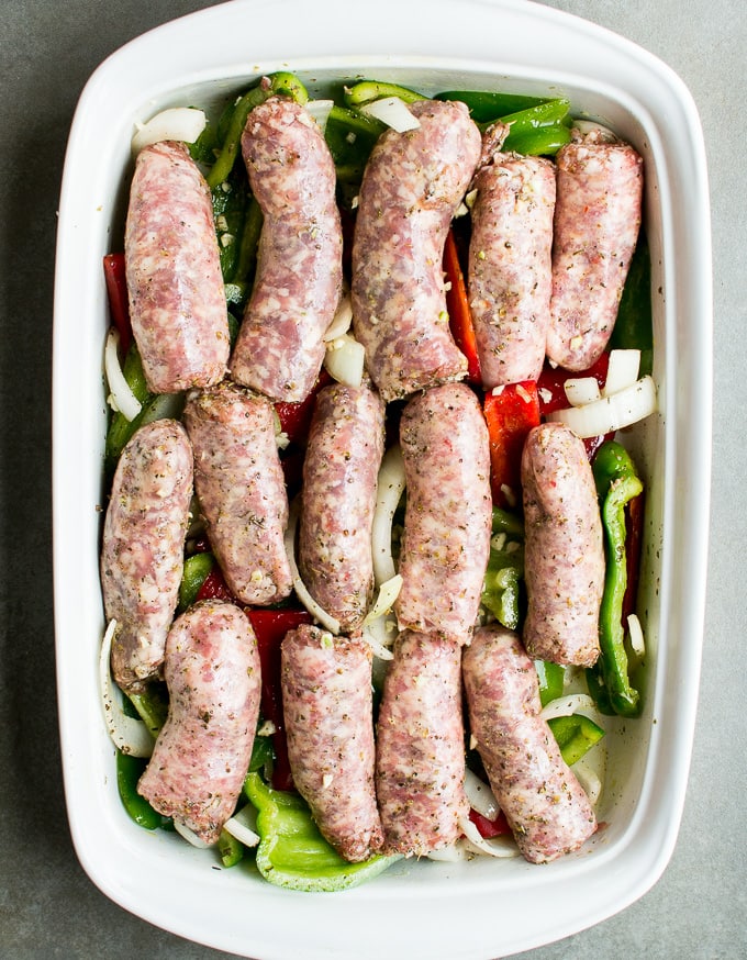 Oven Baked Sausage and Peppers in a white dish, featuring seasoned sausages, green peppers, onions, and tomatoes, ideal for a hearty, flavorful meal.